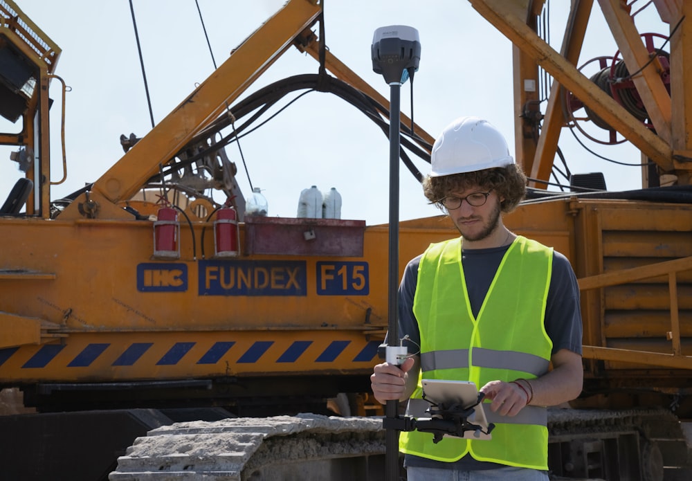 man in green and yellow vest standing beside orange and black heavy equipment