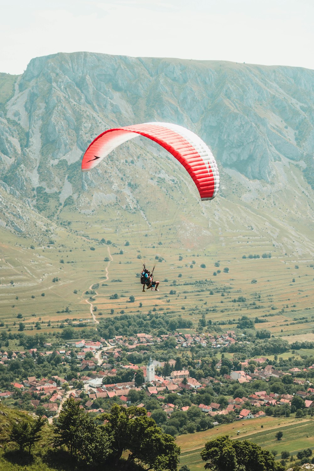 person riding on red and white parachute over green mountains during daytime