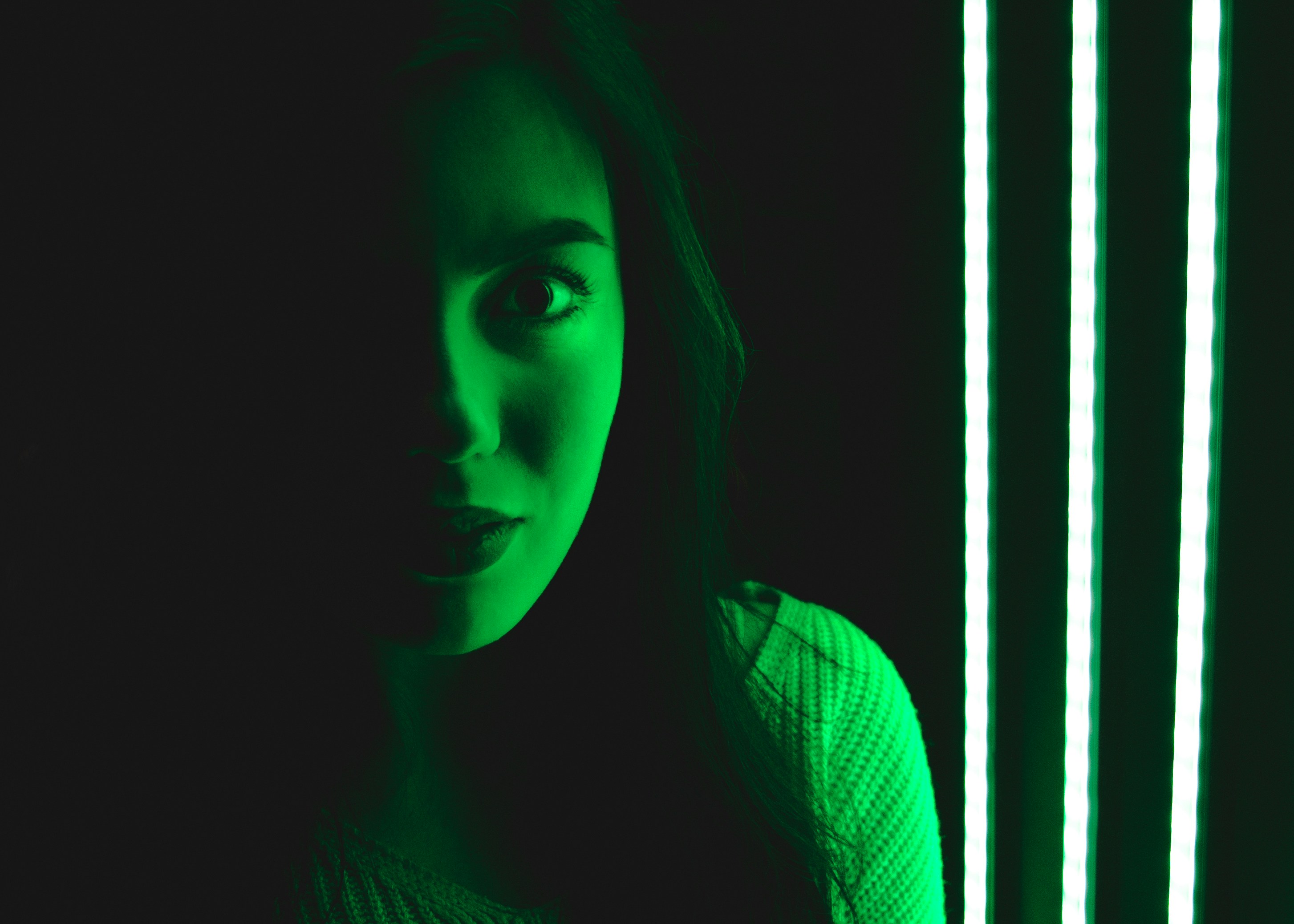 a young woman alarmed illuminated on one side by a green light. say 