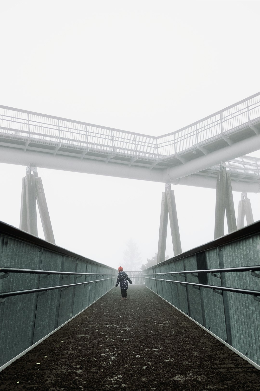 person in red jacket walking on green concrete bridge during daytime