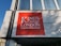 A large red signboard with white text displaying 'King's College London' is mounted on a building with white brickwork. The building features large windows above the sign, reflecting a clear blue sky.