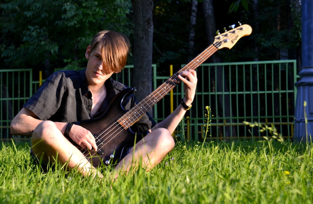man playing guitar sitting on green grass field during daytime