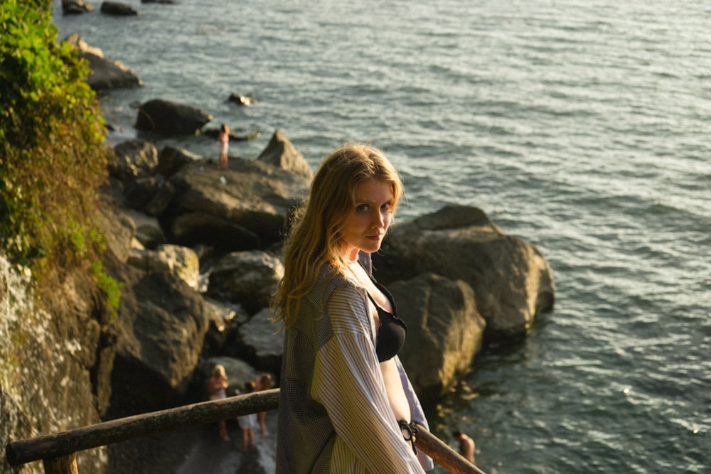 woman in black long sleeve shirt and brown skirt standing on rock near body of water