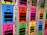 A row of colorful lockers with luggage symbols and numbers on their doors. Each locker is brightly colored in shades such as blue, pink, green, yellow, and orange, and features a large, black suitcase icon. Some lockers have opened red locks hanging on them.