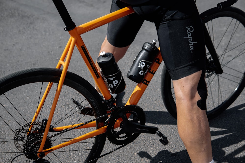 person in black shorts and black nike shoes riding orange and black bicycle