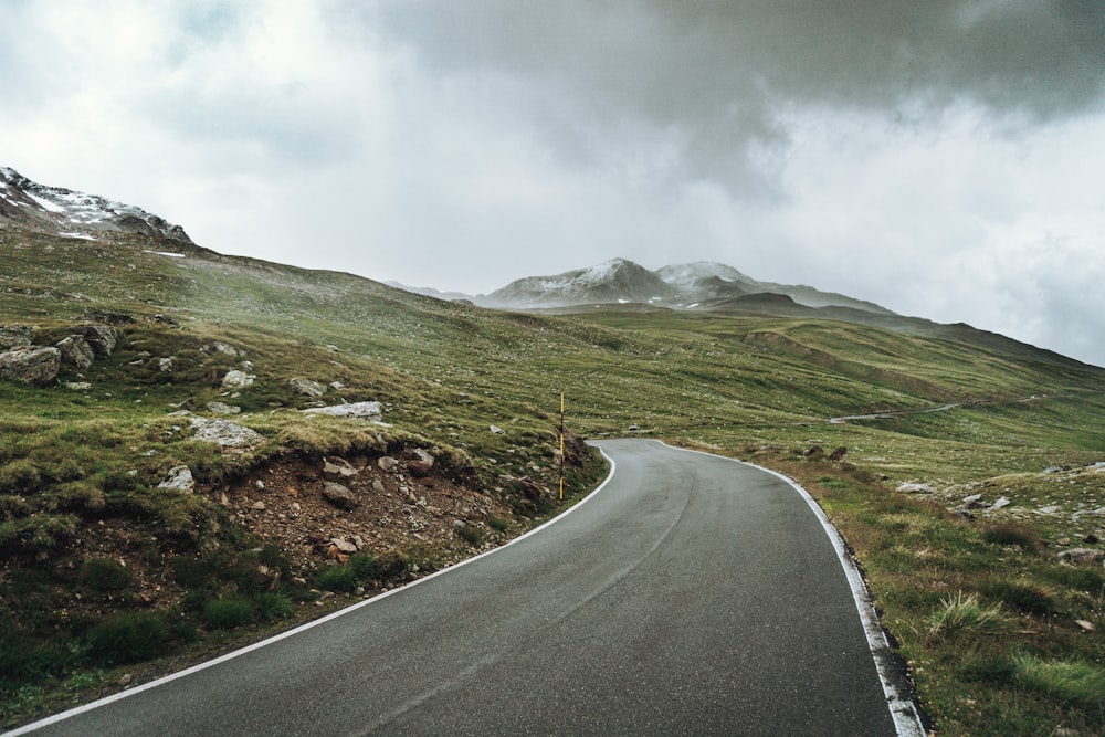 gray concrete road near green grass field and mountain under white clouds during daytime