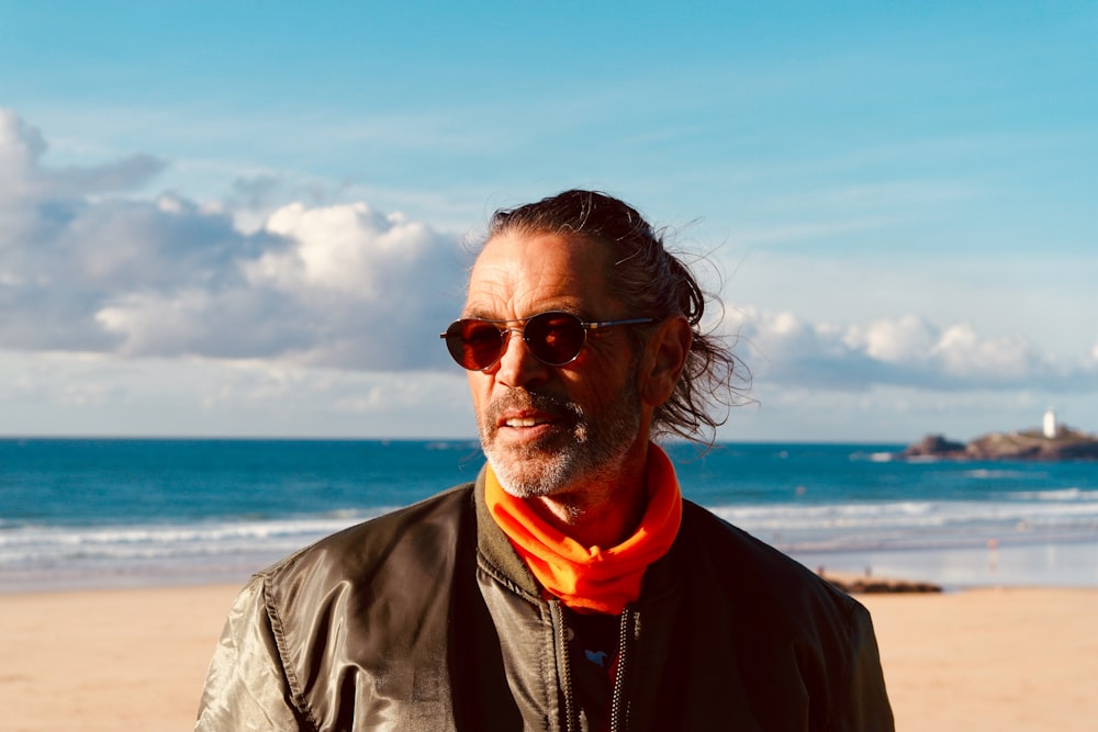 man in black jacket wearing sunglasses standing on beach during daytime