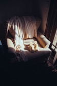 A cozy armchair is bathed in soft, natural light from a nearby window. Draped across the chair is a light-colored, flowing fabric, perhaps a scarf or shawl. A pair of beige, open-toed slippers are neatly placed on the seat, adding to the sense of tranquility and comfort.