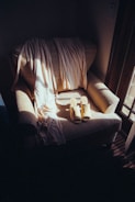 A cozy armchair is bathed in soft, natural light from a nearby window. Draped across the chair is a light-colored, flowing fabric, perhaps a scarf or shawl. A pair of beige, open-toed slippers are neatly placed on the seat, adding to the sense of tranquility and comfort.