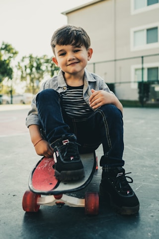 boy in blue denim jacket and blue denim jeans sitting on red round chair