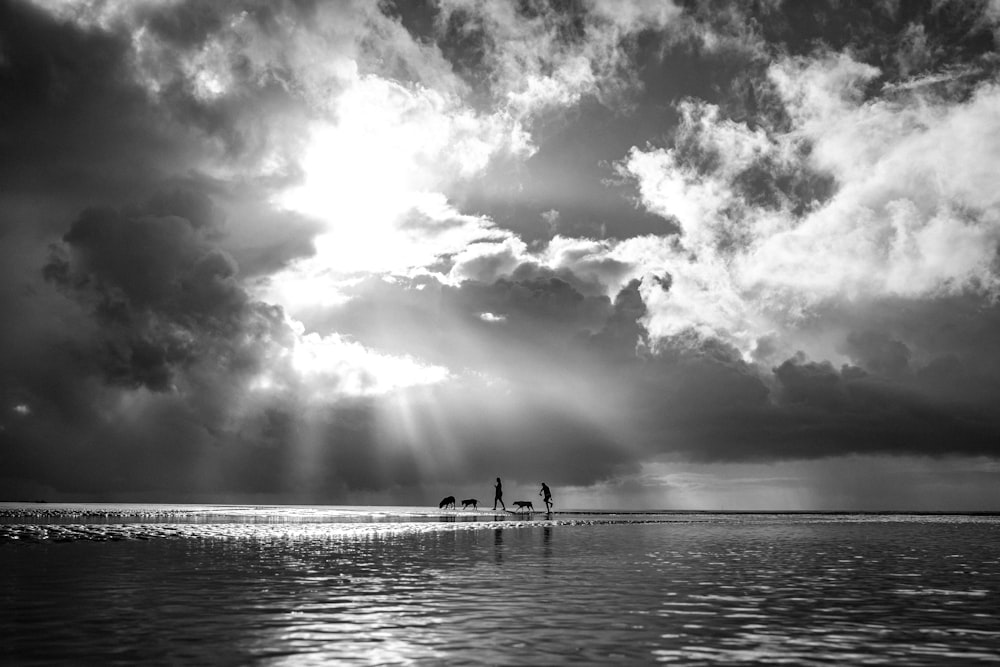 grayscale photo of people on sea under cloudy sky