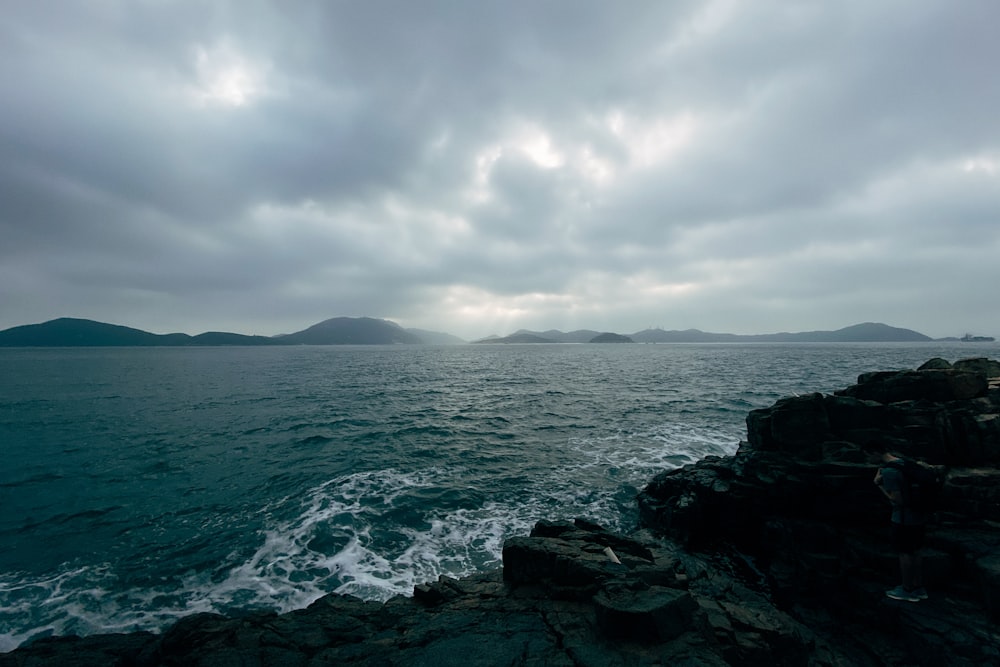 ocean waves crashing on rocks under white clouds during daytime