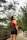 woman in orange tank top and blue denim shorts standing on wooden bridge during daytime