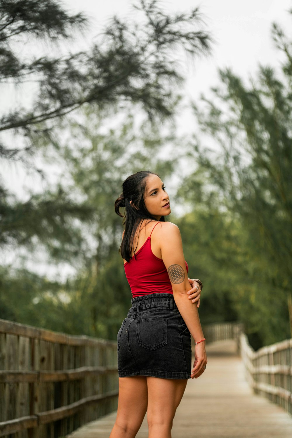 woman in orange tank top and blue denim shorts standing on wooden bridge during daytime