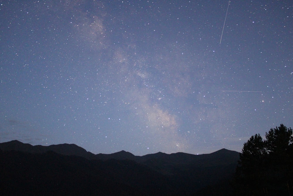 silhouette di montagna sotto cielo blu con stelle durante la notte