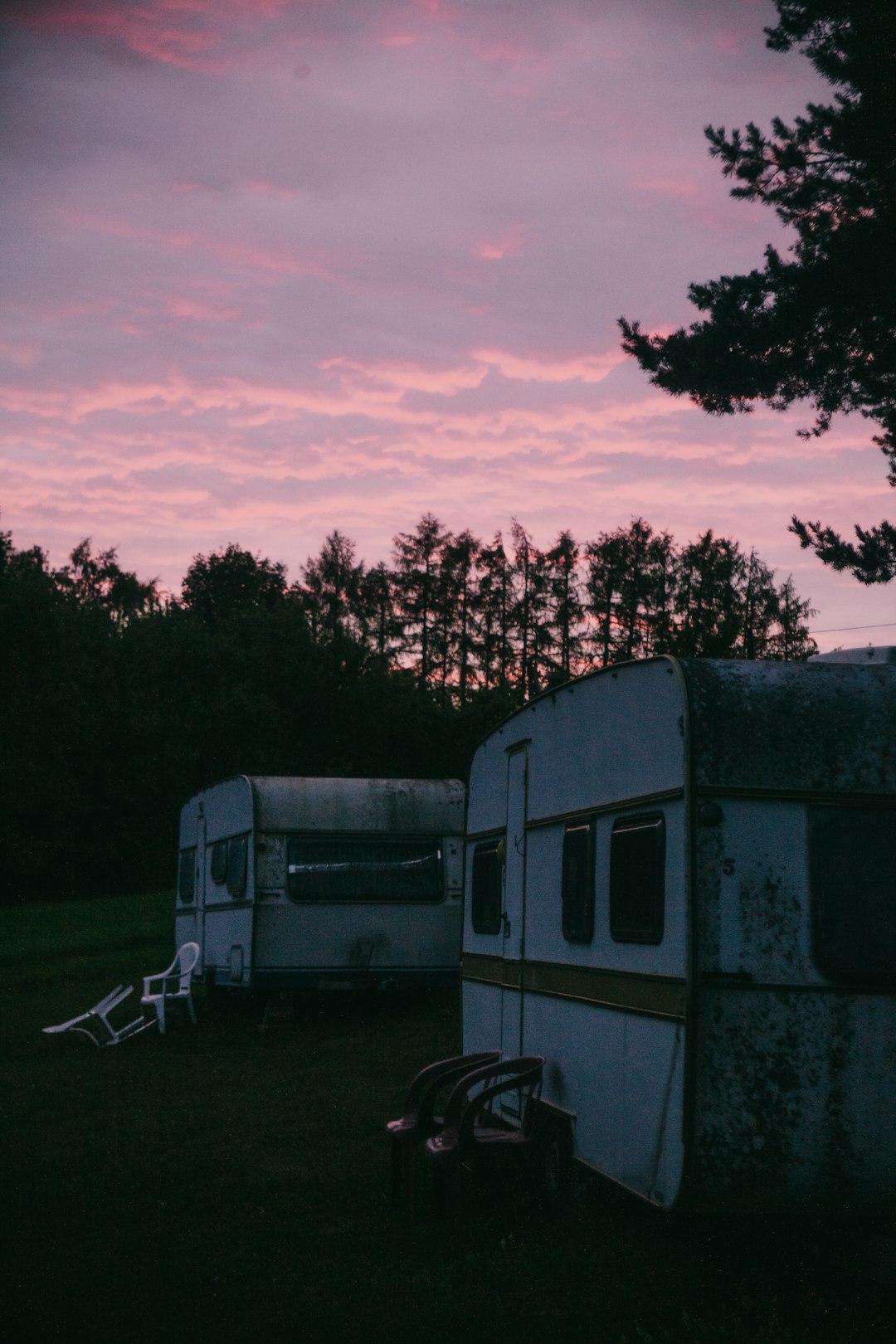 white and black camper trailer on green grass field near green trees under cloudy sky during