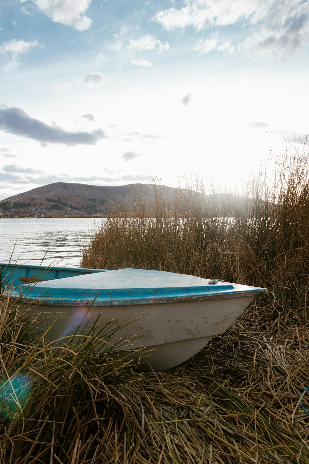 blue and white boat on brown grass field near lake under white clouds during daytime