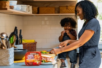 A friendly woman in a cozy kitchen preparing a meal with cleaning supplies nearby.