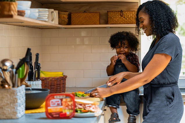 A friendly woman in a cozy kitchen preparing a meal with cleaning supplies nearby.