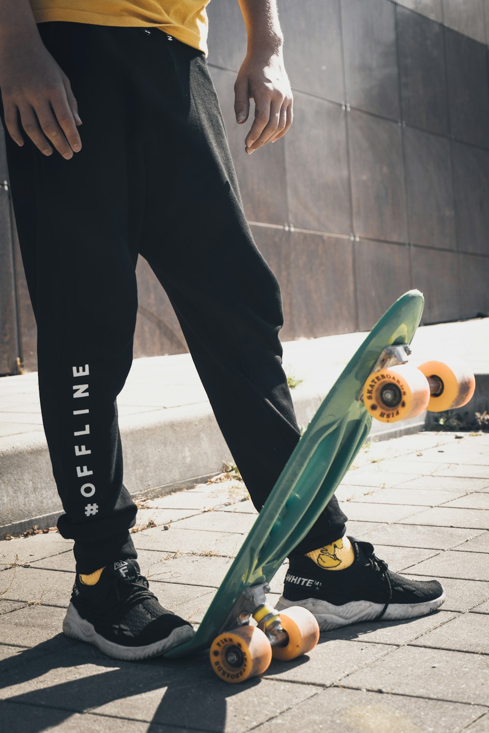 Person in schwarzen Hosen und schwarzen Nike-Schuhen mit grünem Skateboard