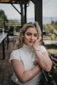 woman in white crew neck t-shirt sitting on brown wooden bench during daytime