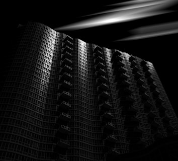 A tall, modern high-rise building with a curved facade and numerous balconies is prominently featured. Dramatic lighting highlights sections of the structure against a dark background, creating an aura of mystery.