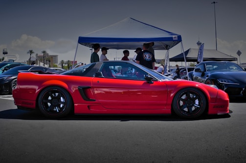 A classic red Pontiac parked under a bright blue sky at a car meet.