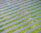 An array of solar panels arranged in parallel rows on a lush green field, capturing sunlight for energy conversion. The solar panels create a pattern of alternating blue and green stripes.