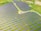 Rows of solar panels are arranged in a large open field, creating a pattern across the landscape. The panels are evenly spaced and set on a grassy terrain with some pathways cutting through the area.
