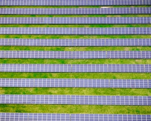 Rows of solar panels are aligned symmetrically over a green grass field, indicating a solar farm designed for harnessing solar energy.