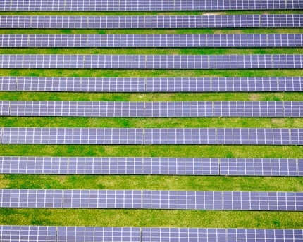 Rows of solar panels are aligned symmetrically over a green grass field, indicating a solar farm designed for harnessing solar energy.