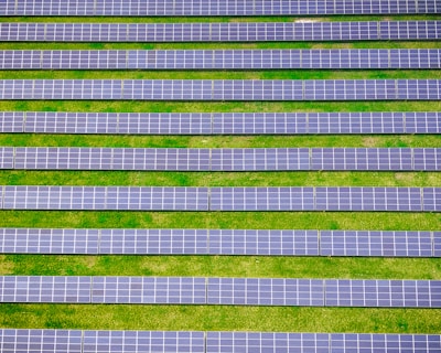 Rows of solar panels are aligned symmetrically over a green grass field, indicating a solar farm designed for harnessing solar energy.