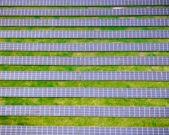 Rows of solar panels are aligned symmetrically over a green grass field, indicating a solar farm designed for harnessing solar energy.