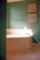 A bathroom corner with a large white bathtub featuring a chrome faucet. The walls are painted green and adorned with two framed artworks, one above the other. A chrome towel bar is also mounted on the wall. Sunlight casts a diagonal shadow across the bathtub and wall.