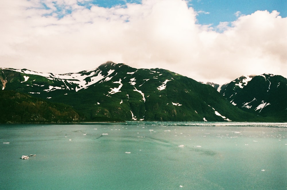 green and black mountain beside body of water under white clouds during daytime