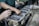 Hands are working on a disassembled engine with visible pistons and connecting rods. One hand is holding a flashlight while another is pointing at a part of the engine.