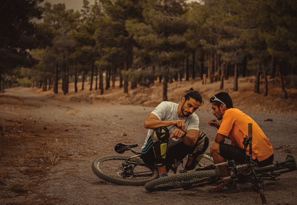 homem na camiseta laranja que monta bicicleta preta ao lado do homem na camiseta branca