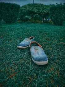 Casual tan loafers paired with rolled-up jeans, placed on a sunlit patio floor with greenery in the background.
