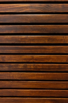 Wooden slats arranged in a horizontal pattern with a rich brown finish, showcasing the natural wood grain and texture.