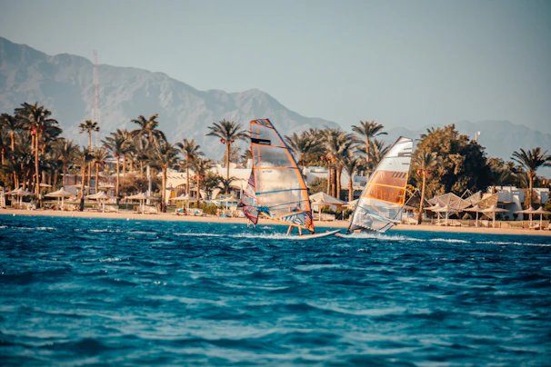 Adventurers enjoying windsurfing on sparkling blue waters with mountains in the background.