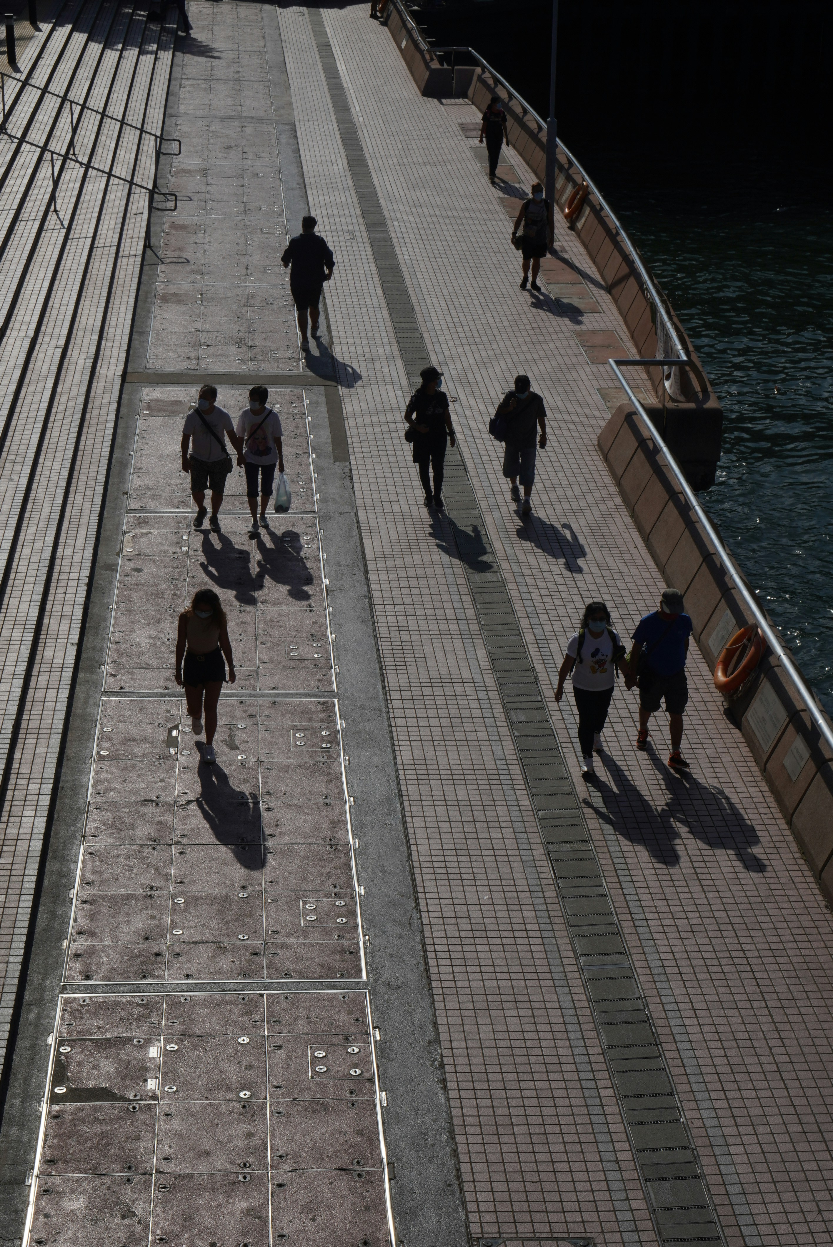 people walking on sidewalk near body of water during daytime