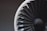A close-up image of a fan blade assembly, likely from a turbine or a model jet engine. The blades are arranged in a circular pattern, with a combination of black and white colors. The background is blurred, focusing attention on the detailed texture and geometric design of the blades.