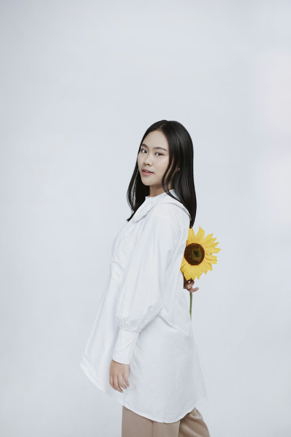 woman in white long sleeve dress holding sunflower
