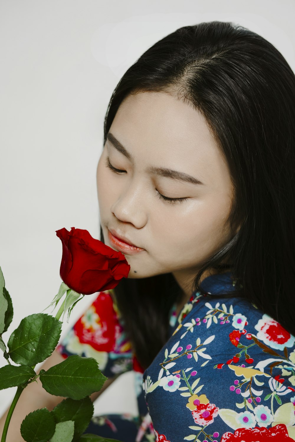 woman in blue and red floral shirt holding red rose
