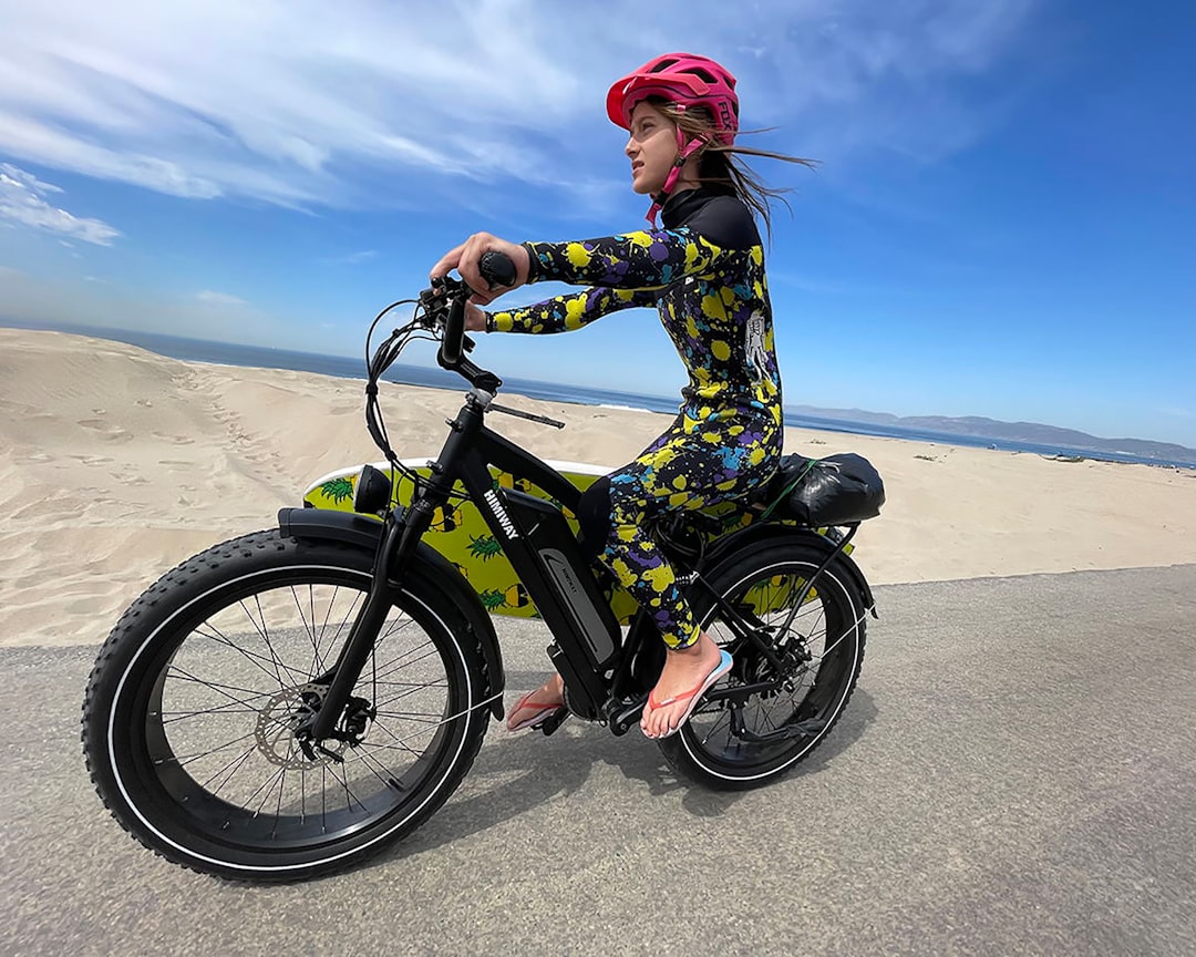 man in green and black camouflage jacket riding on black bicycle on gray sand during daytime