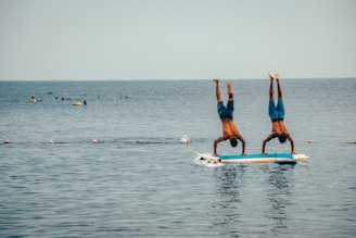 2 women in blue shorts and blue shirt doing yoga on blue surfboard during daytime