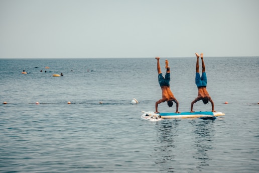 2 women in blue shorts and blue shirt doing yoga on blue surfboard during daytime