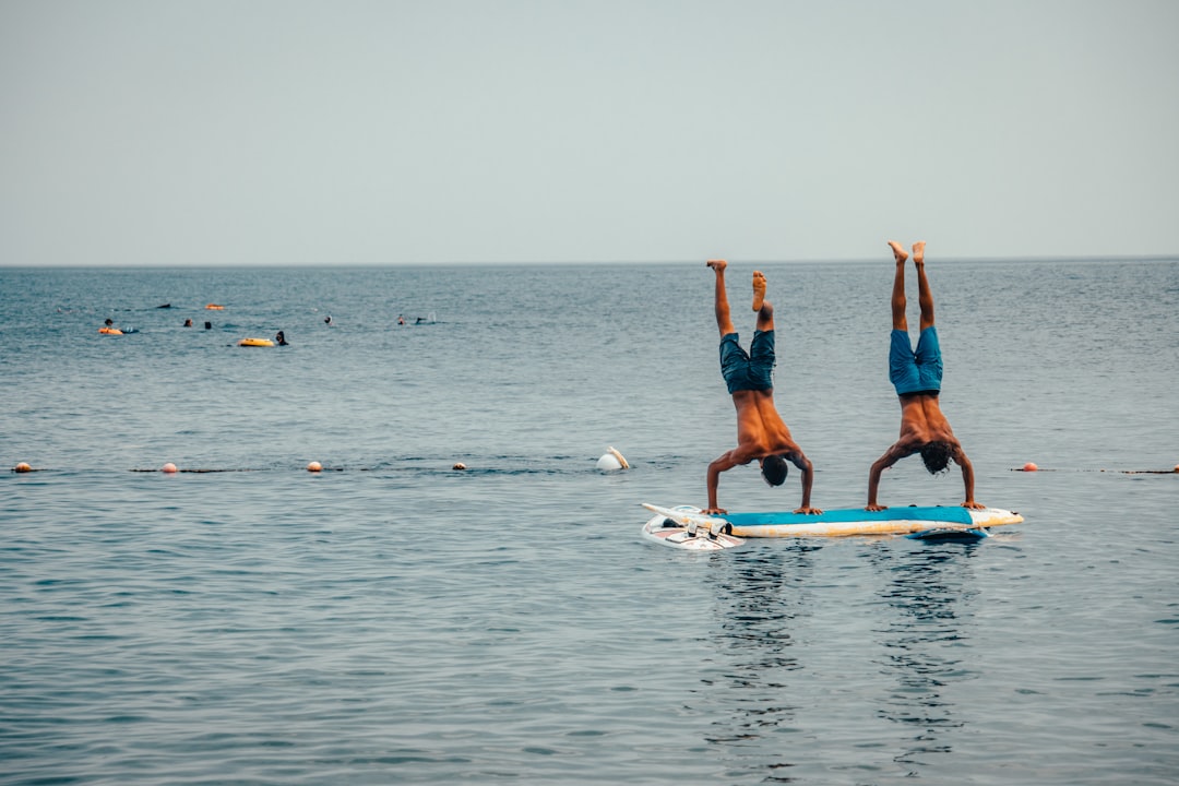 2 women in blue shorts and blue shirt doing yoga on blue surfboard during daytime