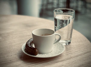 Close-up of a steaming cup of coffee next to a flaky, golden sausage roll on a rustic wooden table.