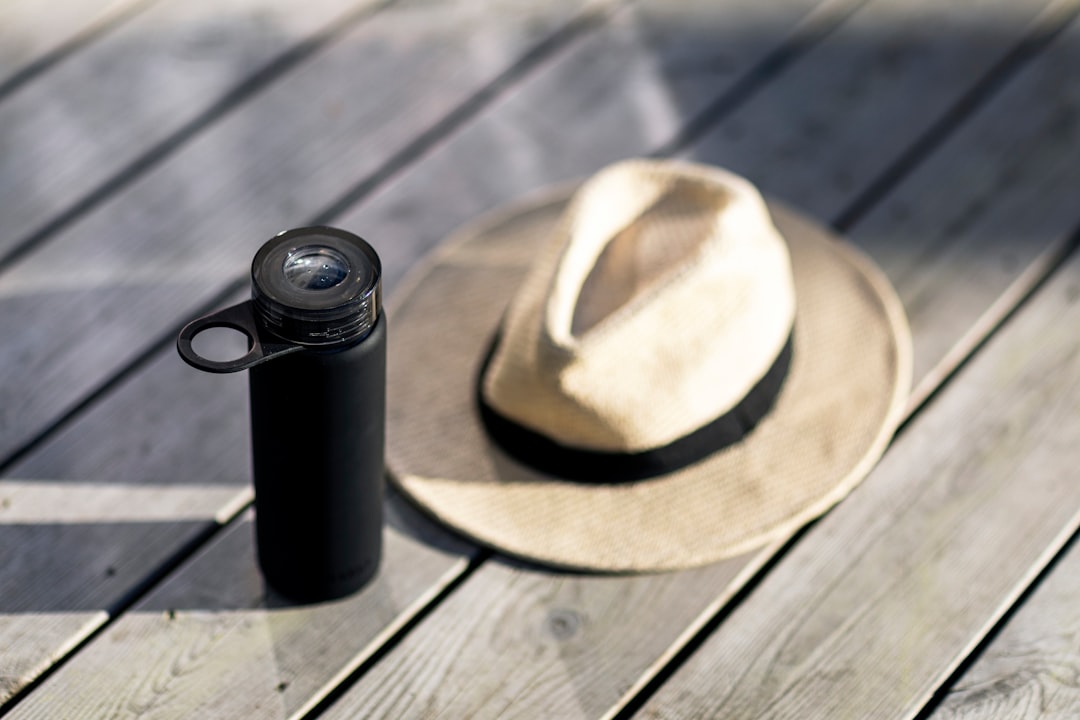 black and brown fedora hat beside black and silver tumbler on brown wooden table